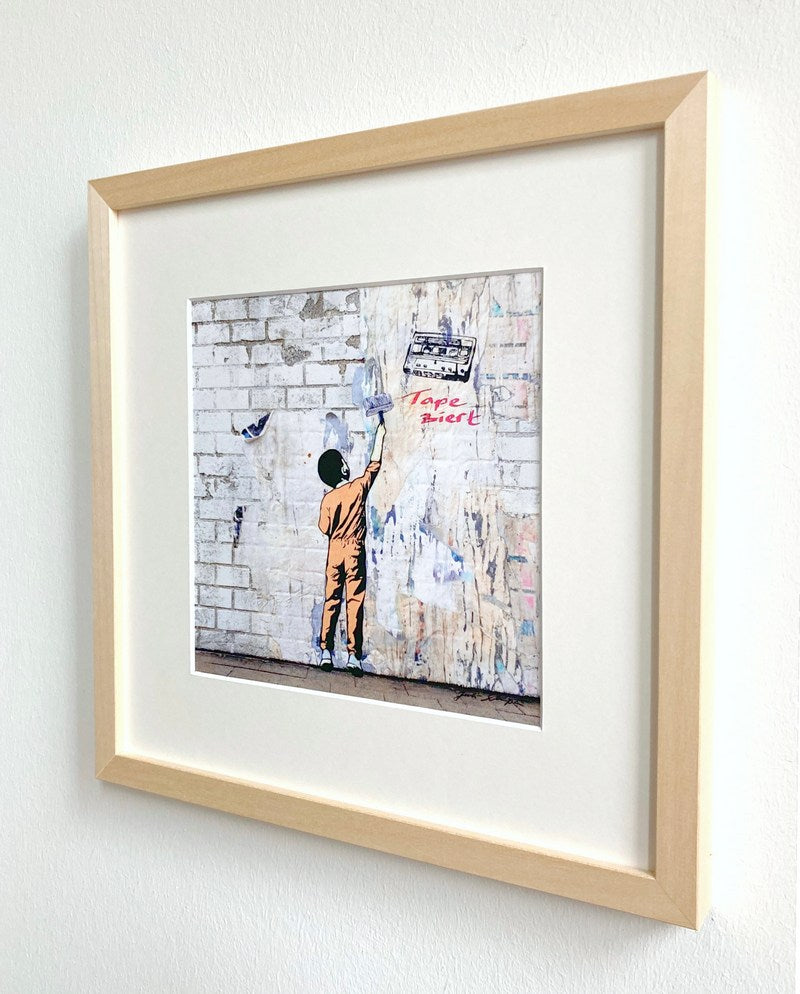 Kunstdruck von Juli Schupa, mit Rahmen und Passepartout, im Motiv ein Junge, der eine Wand taper-ziert, und ein Tape, es ist ein Wortspiel 