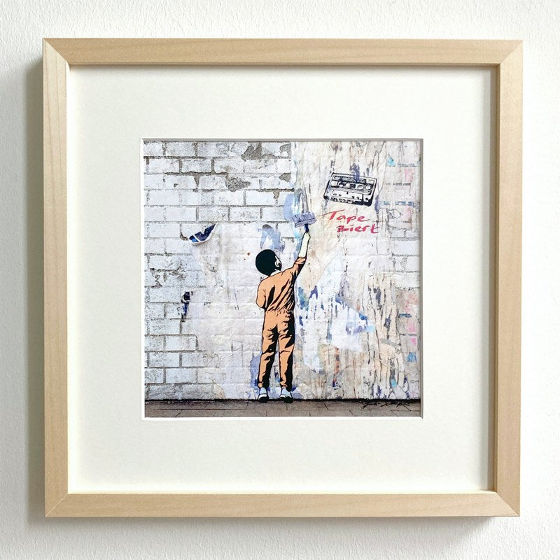 Kunstdruck von Juli Schupa, mit Rahmen und Passepartout, im Motiv ein Junge, der eine Wand taper-ziert, und ein Tape, es ist ein Wortspiel 